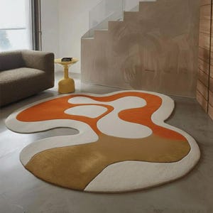 Könnte beinhalten: Ein abstrakter Teppich mit einer einzigartigen, organischen Form. Das Design des Teppichs kombiniert Orange-, Creme- und Beigetöne. Die Kombination aus geometrischen und Freiformen schafft ein ansprechendes Design. Ideal für Wohn- oder Schlafzimmer.