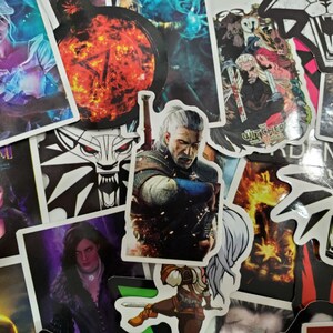 May include: A collection of colorful stickers featuring characters and symbols from the fantasy world of The Witcher. The stickers showcase various characters, including Geralt of Rivia, and the iconic wolf medallion. The stickers are in various shapes and sizes.
