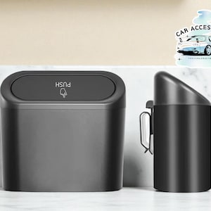 May include: Two black car accessories: a rectangular trash bin with a push-button lid and a cylindrical ashtray with a clip. The trash bin has the word "PUSH" and a hand icon. A sticker with a car graphic is in the background.