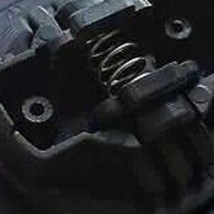 May include: Close-up of a black metal car part with a spring and two small holes. The part appears to be a door lock mechanism.