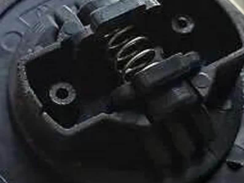 May include: Close-up of a black metal car part with a spring and two small holes. The part appears to be a door lock mechanism.
