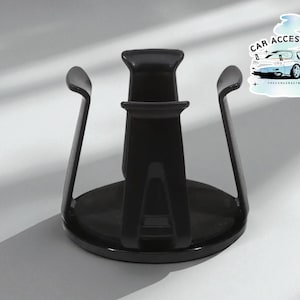 May include: A black car cup holder with a round base and curved arms. The cup holder has a central support and a sticker that says "CAR ACCESSORIES" with a car graphic.