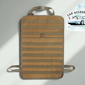 May include: Tan and olive green car seat organizer with multiple horizontal straps for storage. The organizer has a top handle with a buckle and two bottom straps. A sticker with a car graphic and the words "CAR ACCESSORIES" is in the upper right corner.