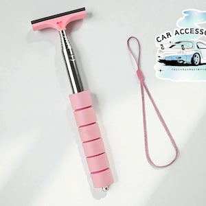May include: A pink car window cleaner with a black rubber blade and a heart-shaped detail. The handle is extendable and has a pink grip. A pink lanyard is also included. The image also includes a sticker that says "CAR ACCESSORIES".