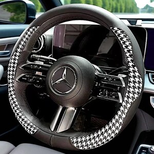 May include: A black and gray steering wheel cover with a houndstooth pattern. The cover is designed to fit a Mercedes-Benz vehicle. The steering wheel has a black center with the Mercedes-Benz logo.