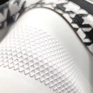 May include: Close-up of a white object with a textured, diamond-patterned surface. A black and white houndstooth pattern borders the object. The image is well-lit, highlighting the details of the design.