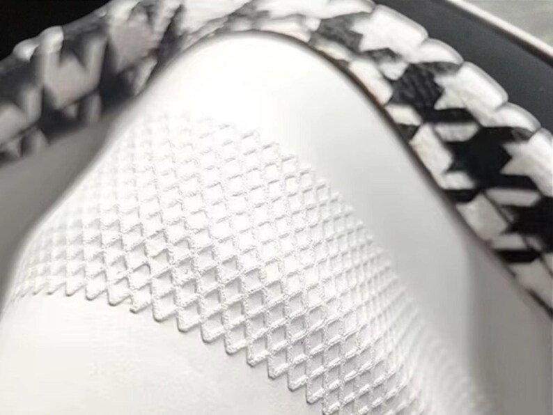 May include: Close-up of a white object with a textured, diamond-patterned surface. A black and white houndstooth pattern borders the object. The image is well-lit, highlighting the details of the design.