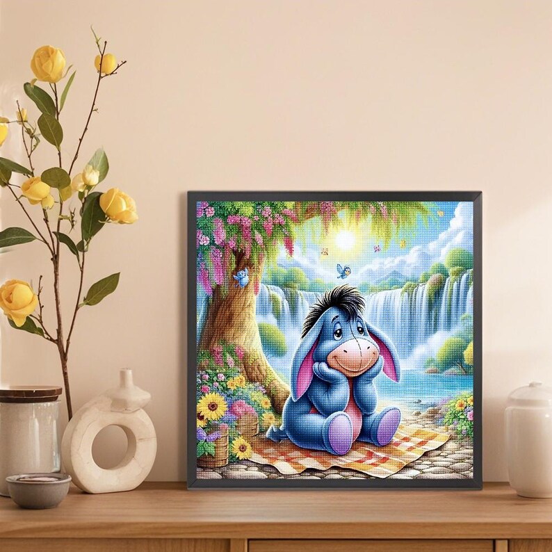 May include: A blue cartoon donkey sits on a checkered blanket in a whimsical forest setting. The donkey is looking down with a thoughtful expression. There is a waterfall in the background and a tree with pink flowers.