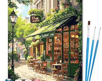 May include: Paint-by-numbers kit featuring a Parisian cafe scene. The image shows a cafe with outdoor seating, a green awning, and the sign "Cafe de Oak". Includes paint pots and three blue-handled paintbrushes.