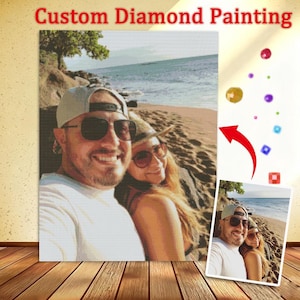May include: A custom diamond painting kit featuring a pixelated image of two people wearing sunglasses and hats on a beach. The text Custom Diamond Painting is at the top. A smaller reference photo shows the original image with colourful diamond beads.