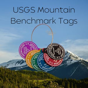 May include: A collection of colorful USGS Mountain Benchmark Tags, each with a unique color and design. The tags are circular and feature text indicating elevation and the U.S. Geological Survey. The background shows a mountain range and blue sky.
