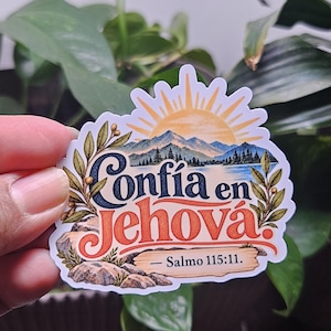 May include: A die-cut sticker featuring a landscape illustration of mountains, a lake, and a sunburst. The text reads Confía en Jehová and Salmo 115:11. The design includes olive branches on the sides and rocks at the bottom in blue, orange, and green.