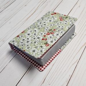 May include: A book cover with a floral pattern featuring white daisies and red strawberries on a green background. The cover is trimmed with a red and white gingham fabric.