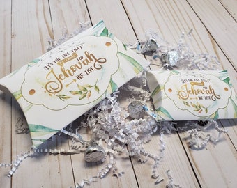 May include: Two white pillow boxes with green and gold watercolor designs. The boxes have the text "It's the life that we choose for Jehovah we live" printed on them. The boxes are filled with white tissue paper and chocolate kisses.