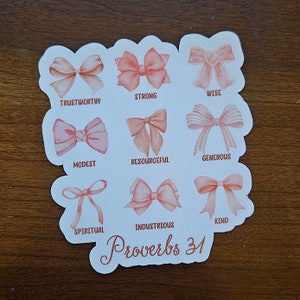 May include: A white sticker with pink bows and the text "Proverbs 31" in brown cursive. Each bow has a word underneath it, such as "Trustworthy", "Strong", "Wise", "Modest", "Resourceful", "Generous", "Spiritual", "Industrious", and "Kind".
