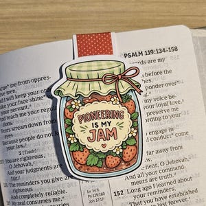 May include: A vibrant sticker depicting a jar of strawberries with the words "PIONEERING IS MY JAM." The jar has a green gingham lid and a pink bow. The sticker is placed on an open book with text from Psalm 119.