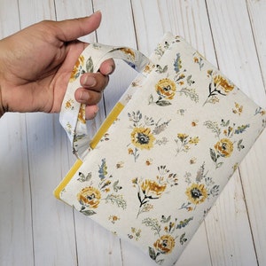 May include: A small, cream-colored fabric bag with a yellow floral pattern and a yellow fabric handle. The bag is made of a soft, lightweight fabric and has a simple, elegant design.