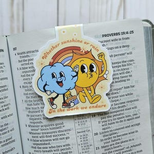 May include: A colourful bookmark featuring a cartoon sun and cloud. The bookmark has the text "Whether sunshine or rain, in the work we endure."