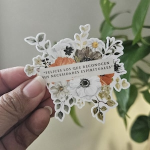 May include: A floral sticker featuring a bouquet of white, orange, and brown flowers with green leaves. A banner across the flowers reads "FELICES LOS QUE RECONOCEN SUS NECESIDADES ESPIRITUALES" with "MATEO 5:3" below.
