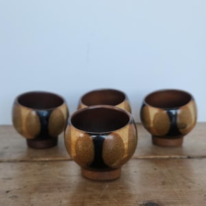 May include: Four wooden bowls with a distinctive design. The bowls have a dark brown base and rim, with a lighter brown and black pattern on the sides. They are arranged on a wooden surface.