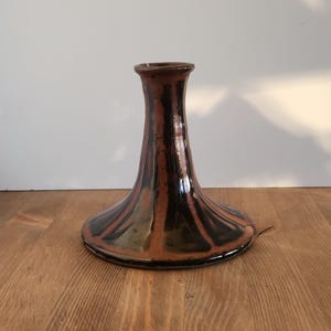 May include: A handmade ceramic vase with a wide base and a narrow neck. The vase features a brown and black color scheme with a glossy finish. The vase is approximately 8 inches tall.