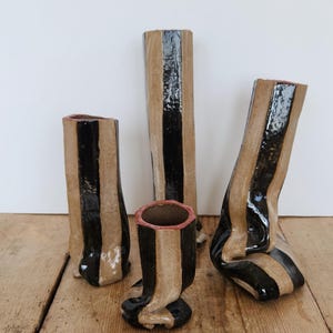 May include: Four ceramic vases with a striped design in black and tan. The vases vary in height and shape, with some leaning or curved. The vases are on a wooden surface.