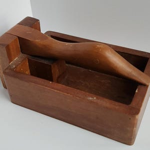 May include: A wooden nutcracker shaped like a bird with a hinged jaw. The nutcracker is made of dark brown wood and has a small compartment for storing nuts.