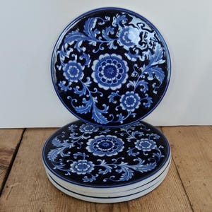 May include: Two round, blue and white ceramic dishes with floral patterns. The dishes have a dark blue background with white floral and leaf designs. The rims are white with a thin blue line.