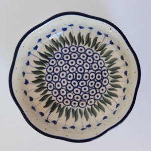 May include: A white ceramic bowl with a blue and green floral design. The bowl has a scalloped edge and is ideal for serving snacks or desserts.