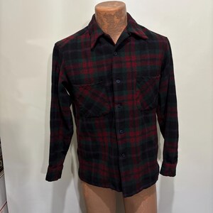Peut inclure: Chemise à carreaux à manches longues dans un motif classique. La chemise présente une palette de couleurs noire, rouge et verte avec deux poches avant et une fermeture boutonnée. La chemise est présentée sur un mannequin.