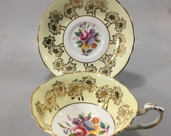 May include: A yellow teacup and saucer set with a floral design and gold trim. The cup and saucer are decorated with a pattern of daisies.