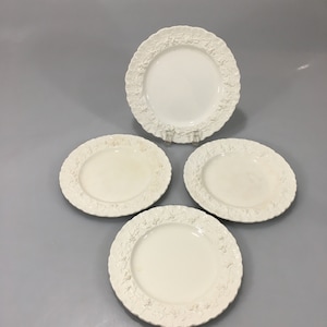 May include: Set of four white ceramic plates with a raised floral design around the rim.