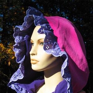 May include: A pink hooded scarf with a purple lining and white lace trim. The scarf is made of a soft, comfortable fabric and has a relaxed, casual style.