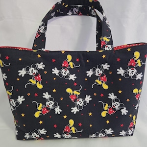 May include: A black tote bag featuring a repeating pattern of Mickey Mouse in various poses, along with yellow and red stars. The bag has red polka dot lining and matching handles.