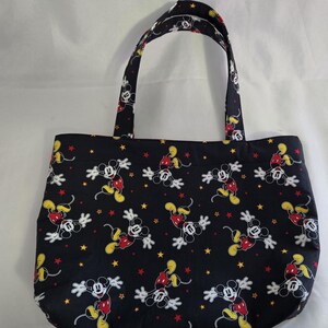 May include: Black tote bag featuring a repeating pattern of Mickey Mouse in various poses with yellow and red stars. The bag has two handles and is made of fabric.
