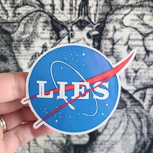 Peut inclure: Un autocollant bleu et rouge avec le logo de la NASA, mais au lieu de "NASA", il dit "LIES".