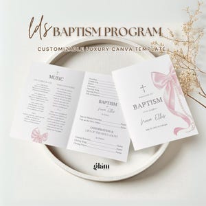 May include: A baptism program template featuring a pink bow and pearl detailing. The program includes text such as "Welcome to Baptism" and "Baptism of Nova Ellis". The program is presented on a white tray with floral decorations.