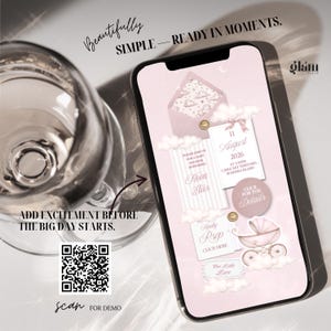 May include: A smartphone displays a baby shower invitation with a pink and white design. The invitation includes the date, time, and location. Text on the screen reads "Nova El&uuml;s", "RSVP", and "Click for the Details". The image also includes a QR code.