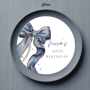 Op de afbeelding: Decoratieve plaat met een blauwe strik en diamantaccenten. De plaat heeft de tekst "Nova's 40th Birthday". De plaat is grijs met een wit midden.