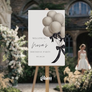 Op de afbeelding: Een welkomstbord voor Nova's verjaardagsfeest, met een tros grijze ballonnen vastgebonden met zwarte linten. Het bord leest "Welkom bij Nova's verjaardagsfeest 05.18.25" in elegant schrift. Het bord wordt weergegeven op een houten ezel.