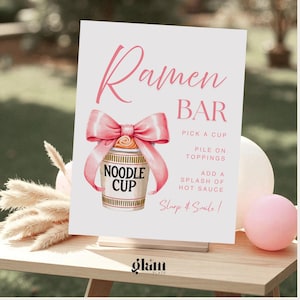 Könnte beinhalten: Ein weißes Schild mit rosa Text, auf dem "Ramen Bar" steht. Es zeigt eine Aquarellillustration einer Nudeltasse mit einer rosa Schleife. Das Schild enthält Anweisungen: "Wähle eine Tasse, gib Toppings drauf, füge einen Schuss scharfe Soße hinzu."