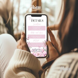 May include: A pink and white mobile phone screen displaying a baby shower invitation with floral accents. The invitation includes the details of the event, including the location, date, and time. The text on the screen reads "The Details", "Location", "Little Bloom Cafe", "Date and Time", "Saturday, February 5th", "3:00 PM", "RSVP", "RSVP by February 5th", "Call or Text 123-456-7890", "Registered at Target & Amazon".