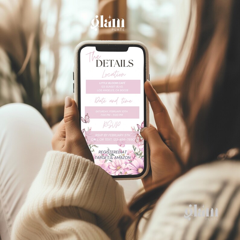 May include: A pink and white mobile phone screen displaying a baby shower invitation with floral accents. The invitation includes the details of the event, including the location, date, and time. The text on the screen reads "The Details", "Location", "Little Bloom Cafe", "Date and Time", "Saturday, February 5th", "3:00 PM", "RSVP", "RSVP by February 5th", "Call or Text 123-456-7890", "Registered at Target & Amazon".
