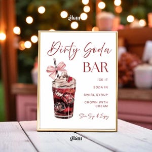 May include: A framed sign with the words "Dirty Soda Bar" in burgundy script. The sign features an illustration of a soda with ice, whipped cream, and a raspberry. Instructions include "Ice it, Soda in, Swirl Syrup, Crown with Cream."