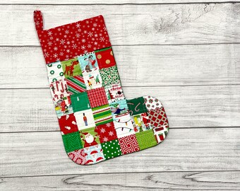May include: A quilted Christmas stocking with a red cuff featuring white snowflakes. The body of the stocking is a patchwork of various Christmas-themed fabrics, including Santa Claus, candy canes, and reindeer. The stocking has a red loop for hanging.