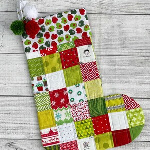 May include: A red and green patchwork Christmas stocking with a white cuff featuring a green and red mitten pattern. The stocking has a white pom-pom on top and the text "cute monsters" is visible on the side.