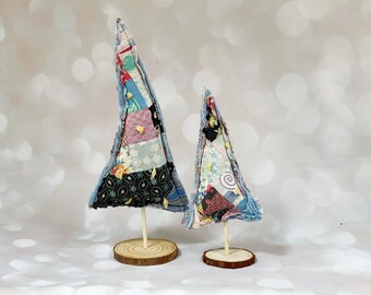 May include: Two fabric Christmas trees, one larger than the other, are made of patchwork fabric in shades of blue, pink, and green. They are standing on wooden bases.