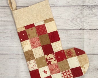 May include: A red and cream patchwork Christmas stocking with a cream fabric cuff. The stocking is made of squares of different fabrics with floral and geometric patterns.