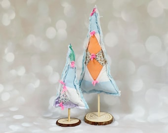 May include: Two handmade fabric Christmas trees, one larger than the other, with a blue and white patchwork design and pink bows. The trees are on wooden bases.