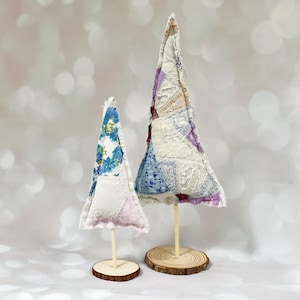 May include: Two fabric Christmas trees on wooden bases. The larger tree is made of white fabric with purple, blue, and pink floral patterns. The smaller tree is made of white fabric with blue floral patterns.
